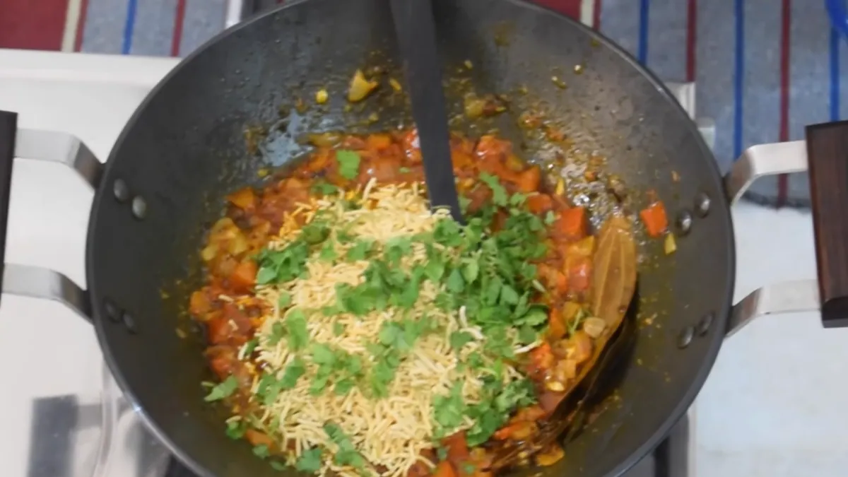 Kadhai me taiyaar Sev Tamatar ki Sabji — tamatar ki gravy par sev aur hara dhaniya, serve karne se theek pehle